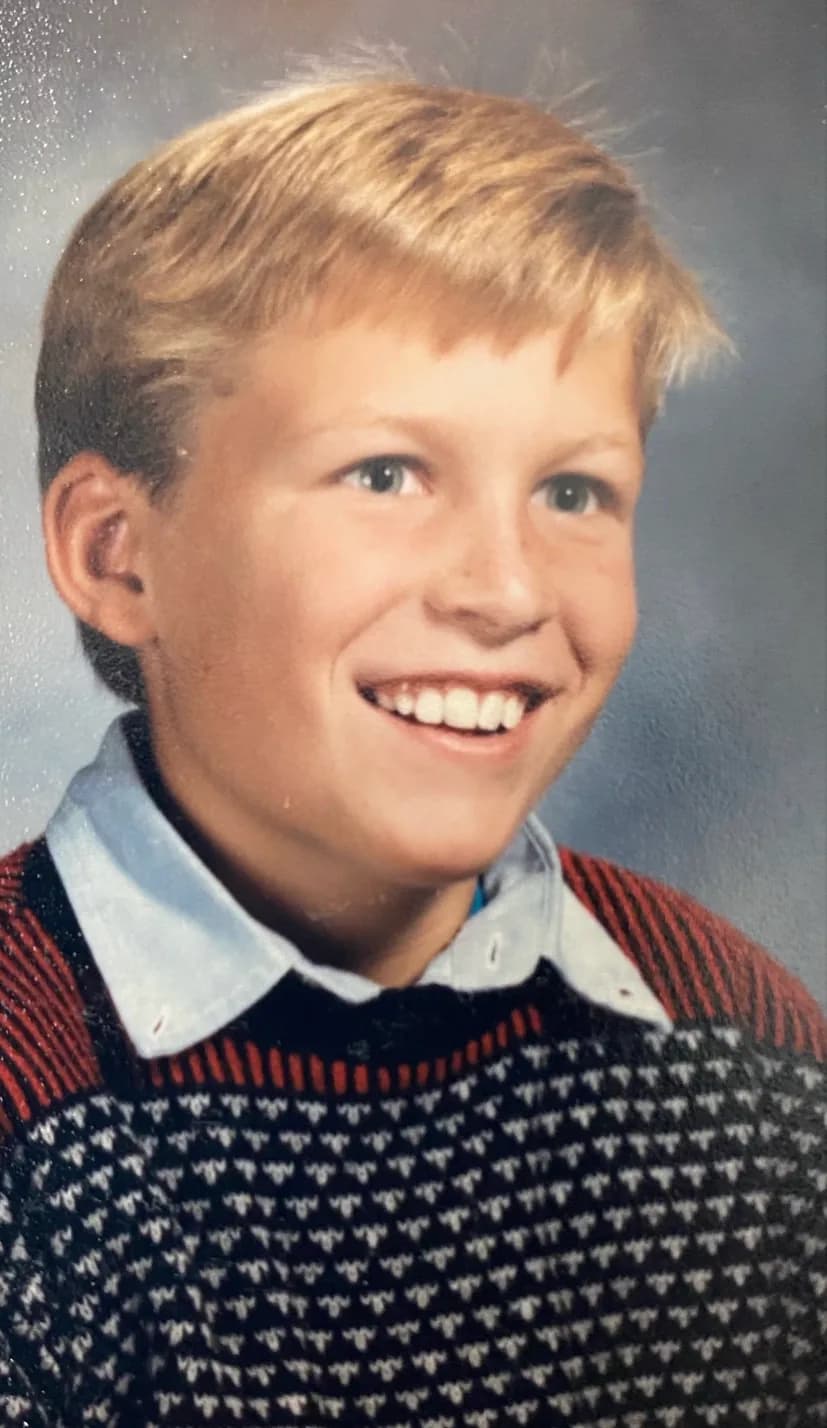 A school portrait of Brannon as a boy, fair haired, in a collared shirt and patterned sweater.