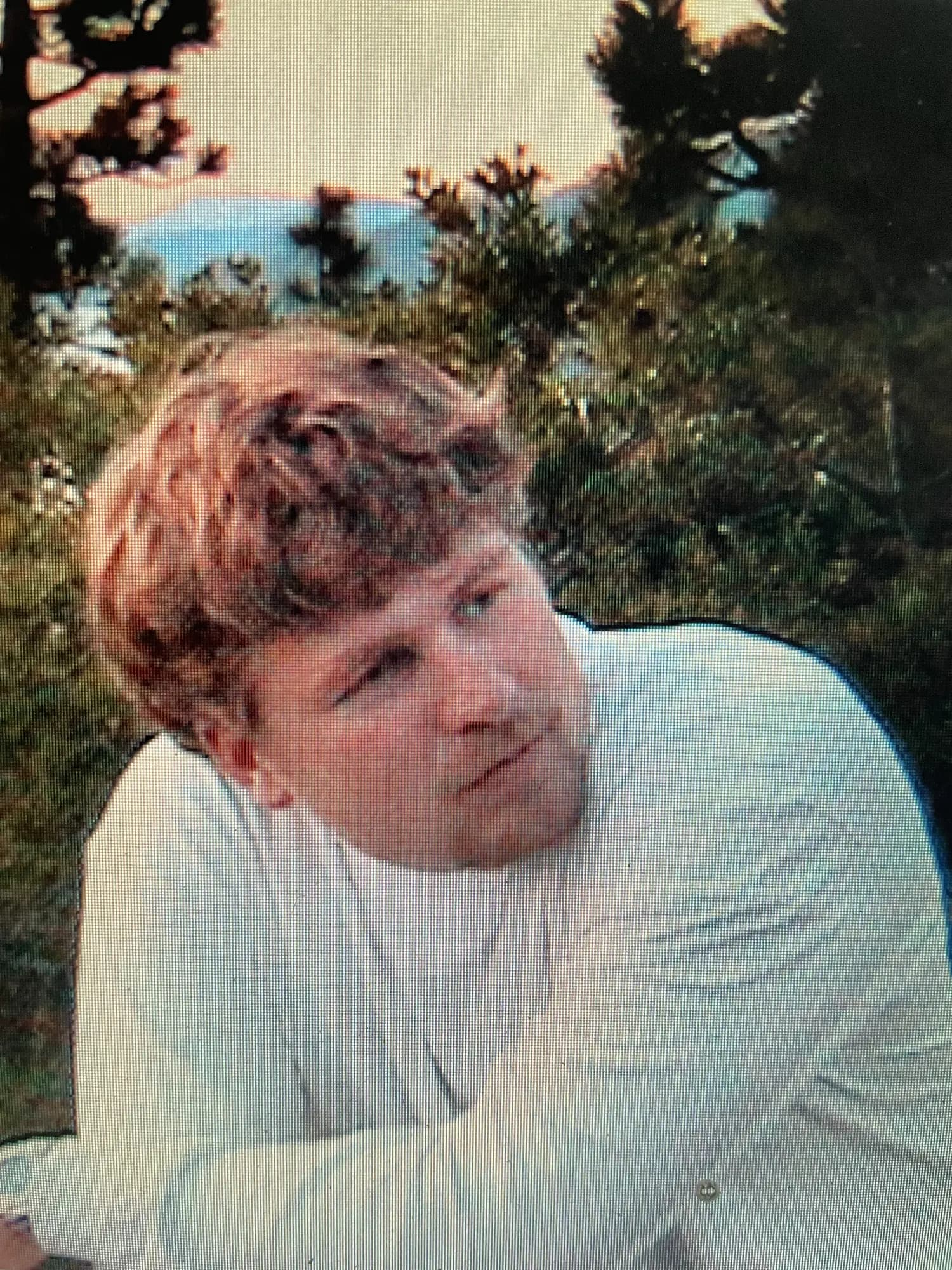 Brannon as a teenager outdoors in a white long sleeved shirt, leaning on his arms with trees behind him.