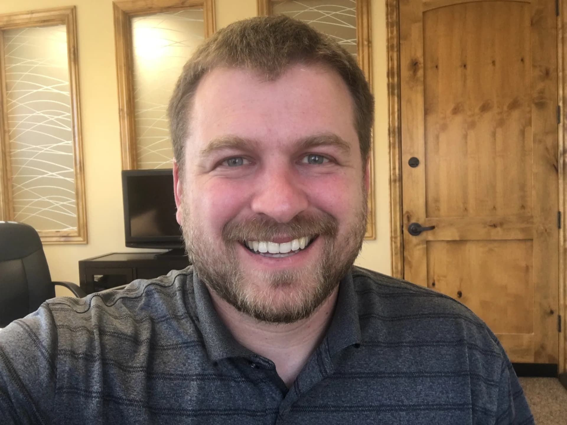 Brannon smiling in a therapy office, a wooden door and framed glass panels behind him.