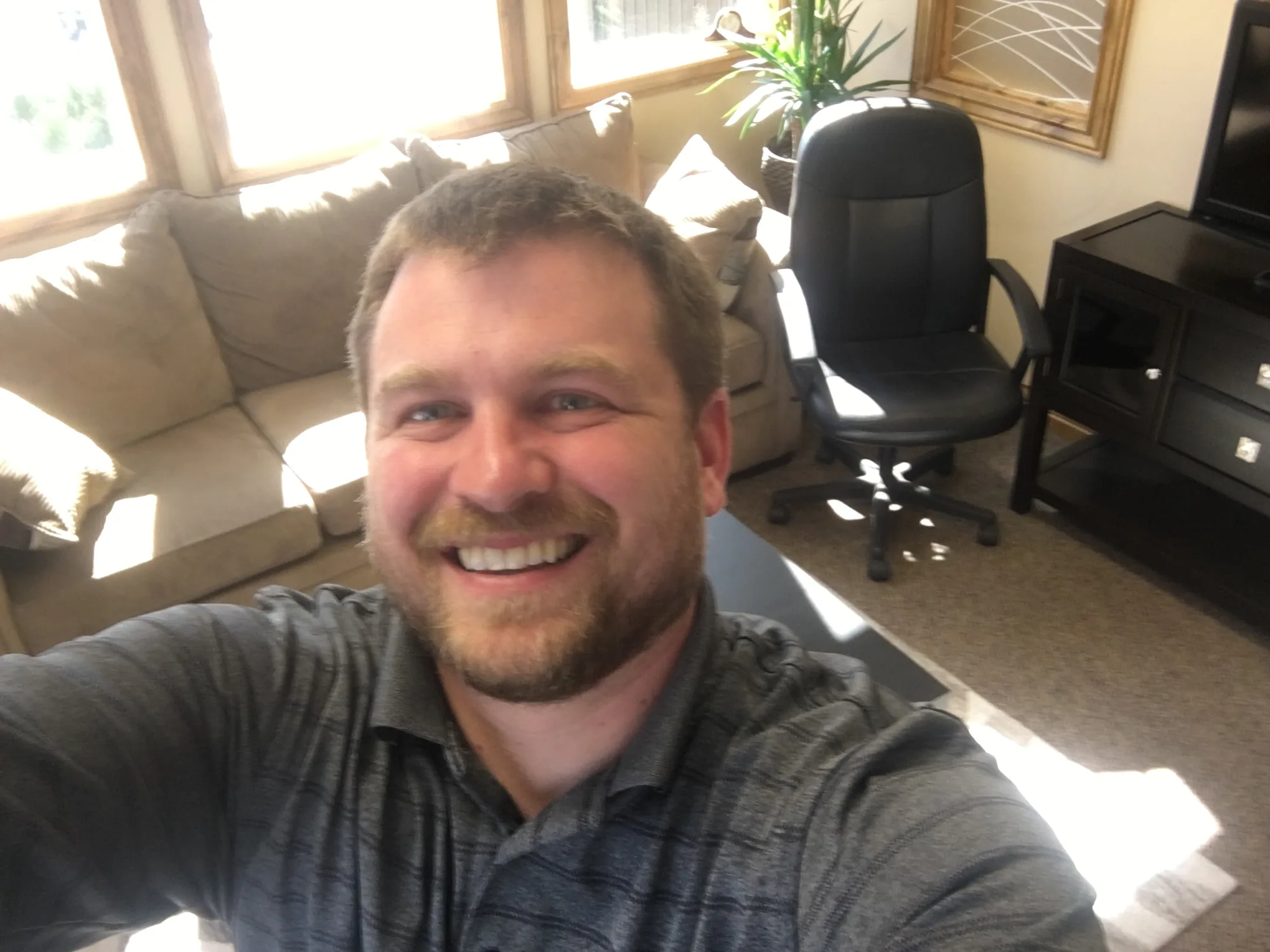 Brannon smiling in his office, with a couch, an office chair and a window behind him.