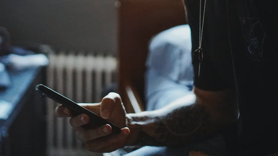 A pair of hands holding a lit phone in a dark room, the face out of frame.